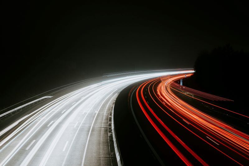 this image captures a long-exposure photograph of a motorway at night. the photo shows two sets of light trails created by vehicles: white light trails on the left and red light trails on the right. 